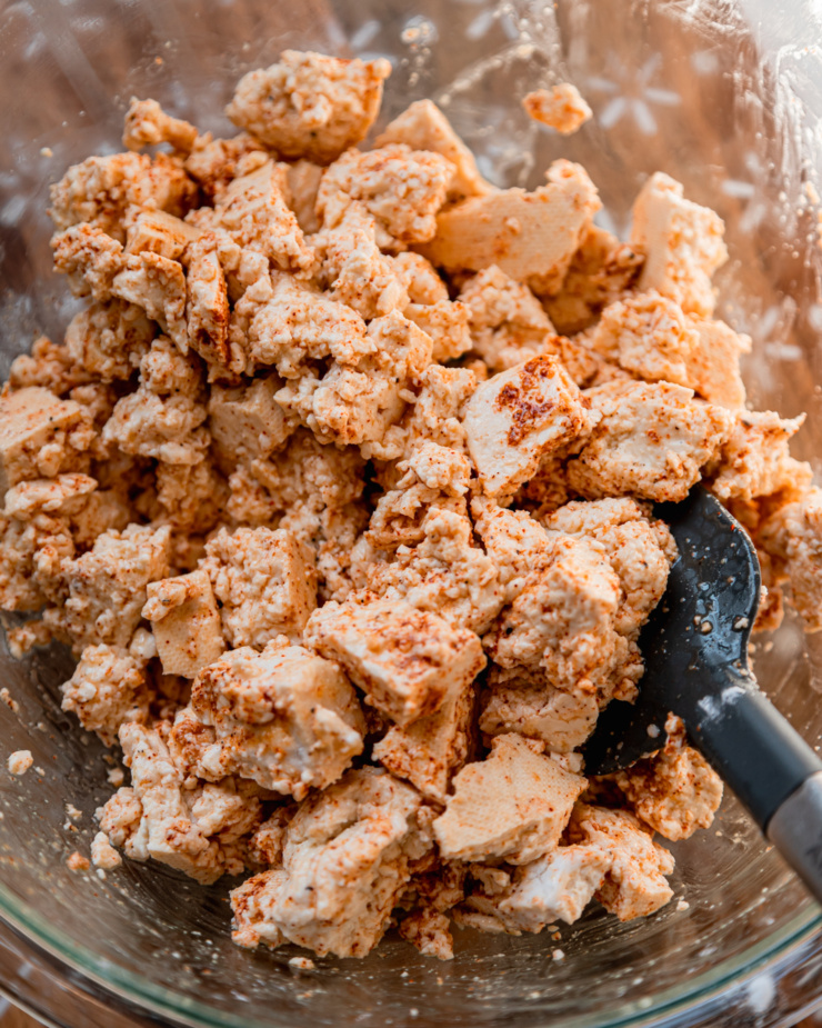 An overhead shot shows pieces of tofu tossed with oil, spices, and arrowroot starch.