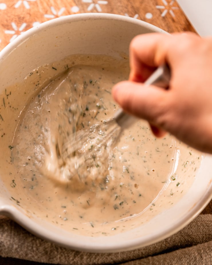 An overhead shot shows a hand using a whisk tobring a creamy dressing together in a mixing bowl.