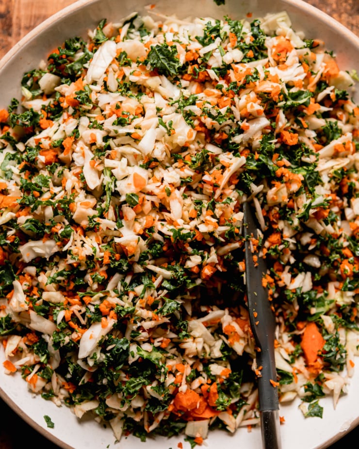 An up close, overhead shot shows finely chopped cabbage, kale, and carrots in a wide bowl.