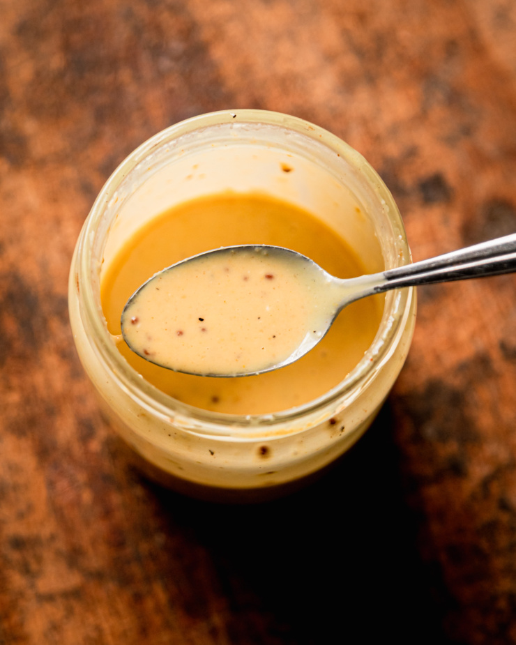 An overhead shot shows a creamy sweet mustard dressing in a jar with a spoonful being lifted out of the jar.