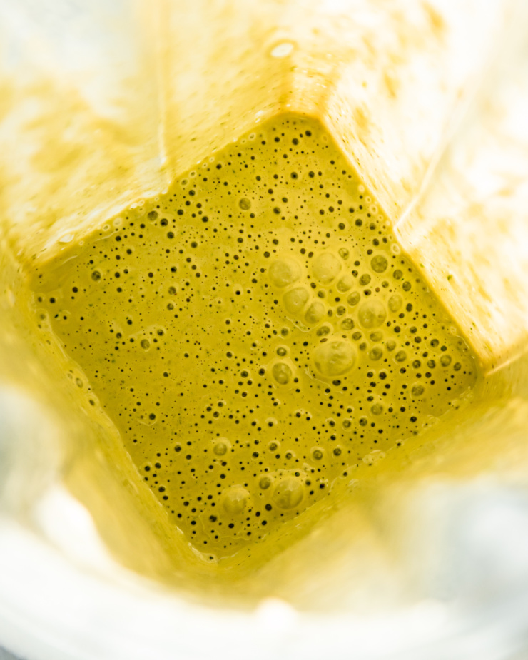 An overhead shot shows a blended up dilly tahini sauce in a blender pitcher. The consistency is creamy.