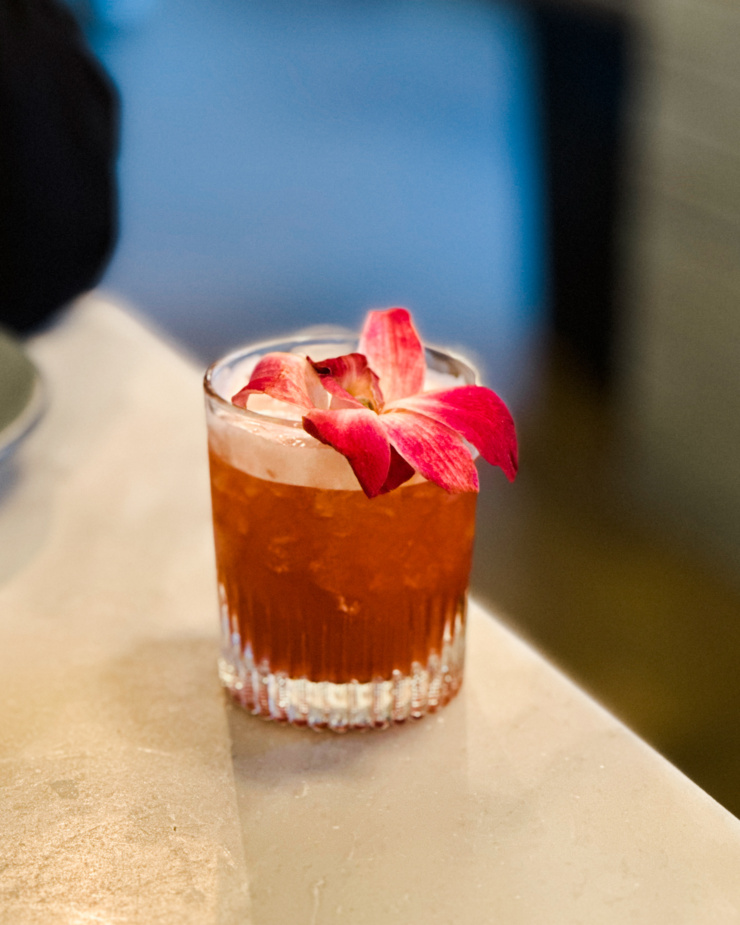 A head-on shot shows a frothy pink beverage in a glass garnished with an orchid flower.