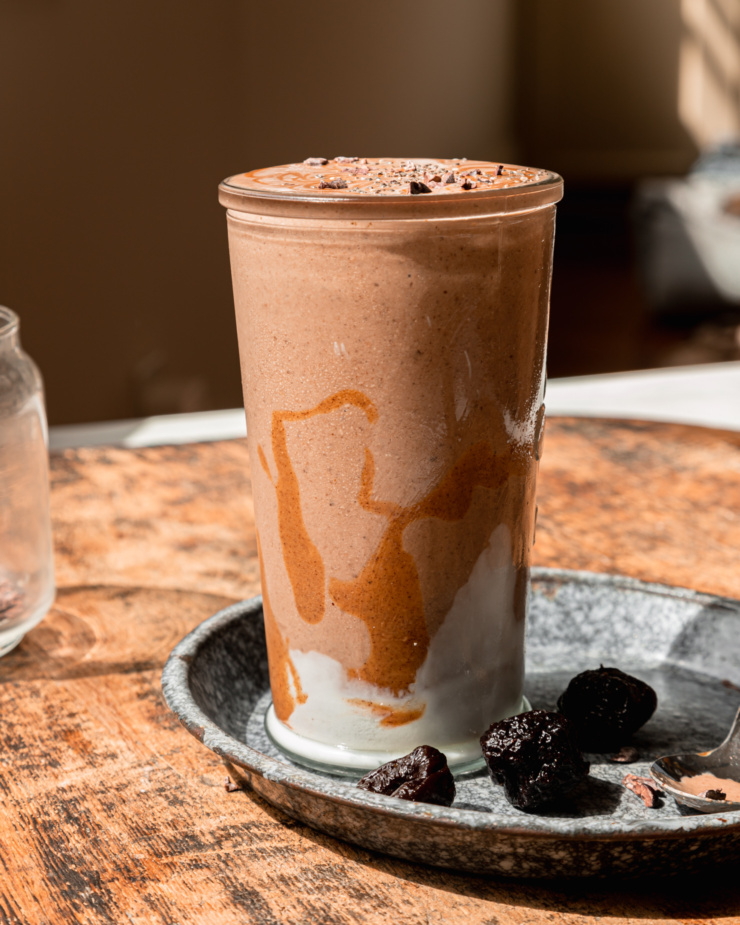 A head-on shot shows a glass of vegan chocolate fantasy smoothie with swirls of almond butter and vegan yogurt on the side of the glass.