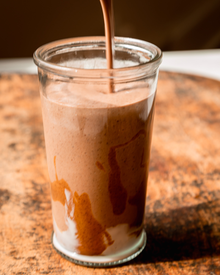 A chocolaty smoothie is being poured into a glass.