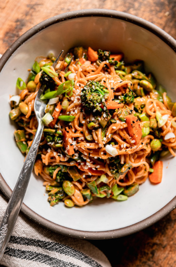 An overhead shot shows an individual bowl serving of veggie-filled vegan Gochujang noodles. A fork is sticking out of the noodles.