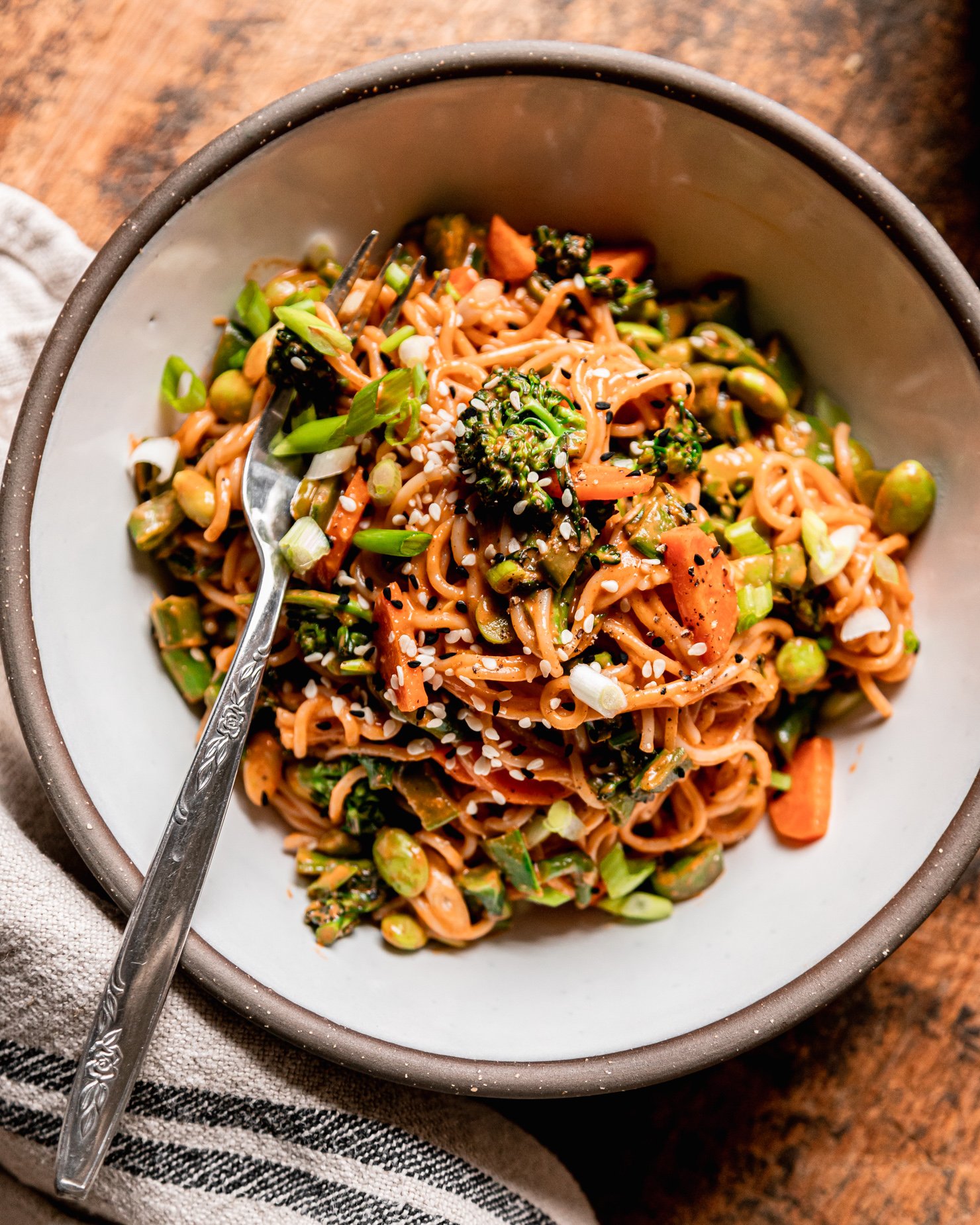 An overhead shot shows an individual bowl serving of veggie-filled vegan Gochujang noodles. A fork is sticking out of the noodles.