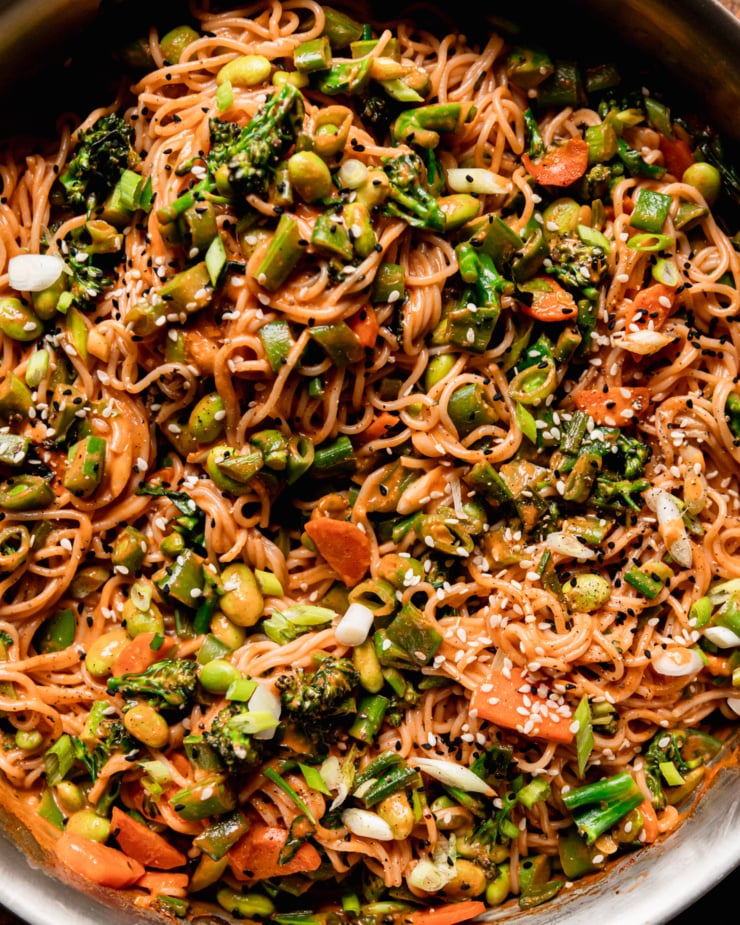 An up close, overhead shot shows a bunch of vegan Gochujang noodles with lots of sautéed chopped vegetables. The noodles are garnished with sliced green onions and sesame seeds.