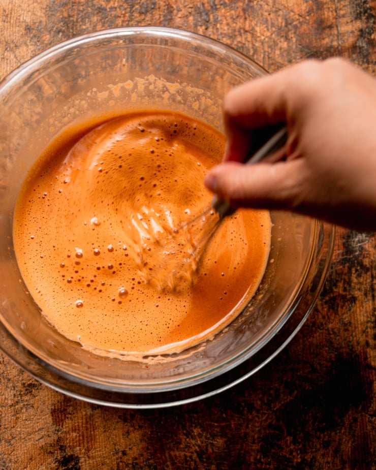 An overhead shot shows hand using a whisk to mix up a Gochujang noodle stir fry sauce.
