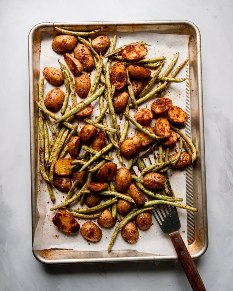 An overhead shot shows a baking sheet with roasted halved baby potatoes and green beans.