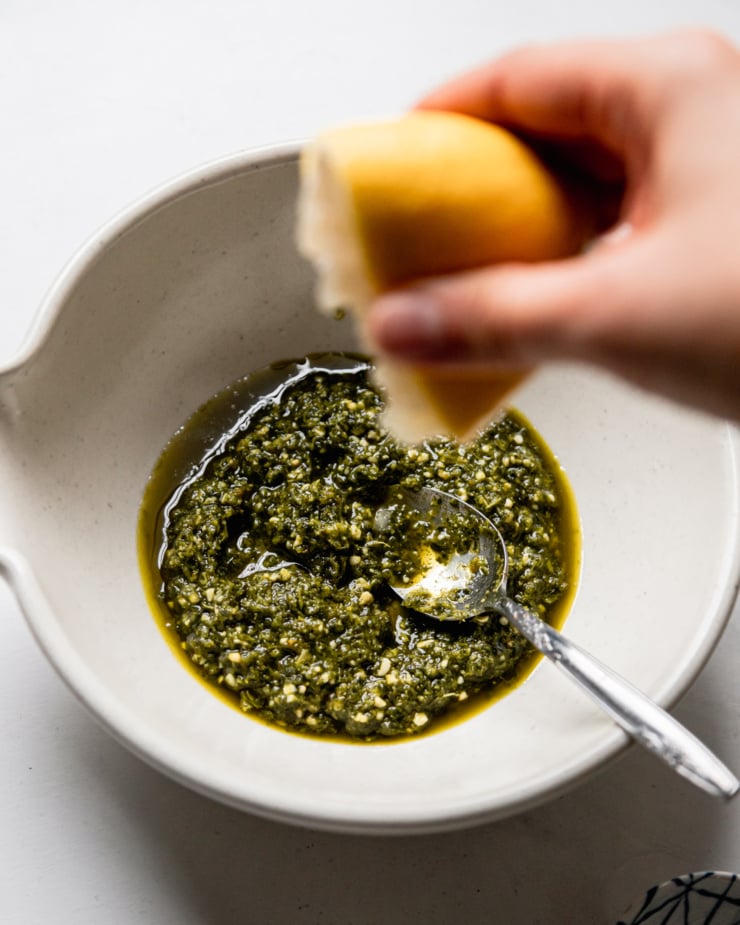 An overhead shot shows a lemon being squeezed into a small bowl of vegan pesto.