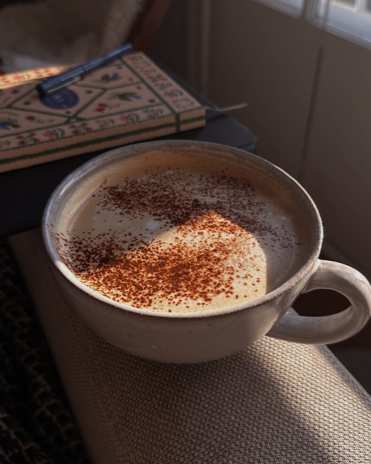A head-on shot shows a café au lait in a wide mug resting on the arm of a couch.