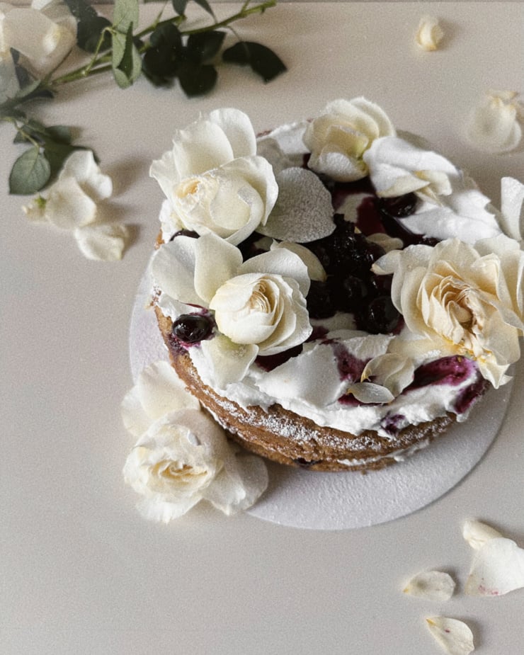An overhead shot shows a beautiful cake decorated with coconut cream, lavender blueberry compote and white roses.