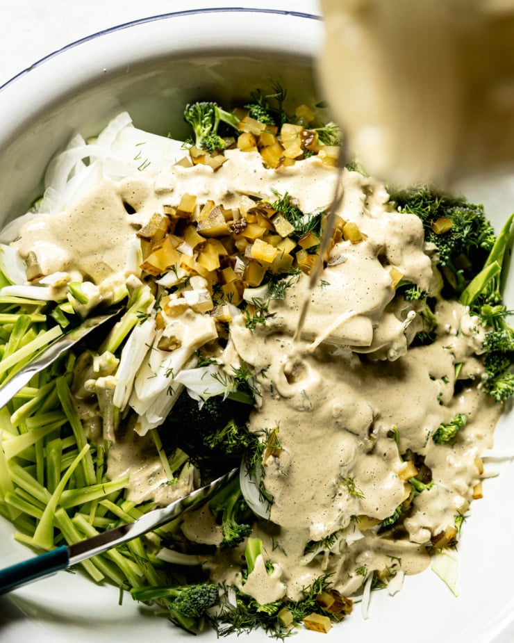 An overhead shot shows a creamy dressing being poured over all of the prepped vegetables and herbs.