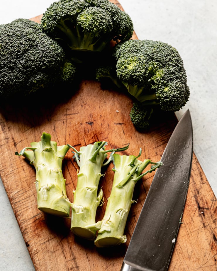 An overhead shot shows broccoli florets and stalks, cut away from each other on a cutting board.
