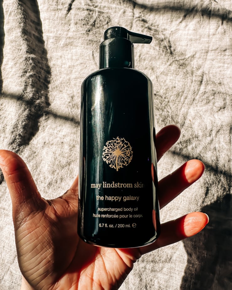 An overhead shot shows a hand holding a bottle of May Lindstrom body oil.