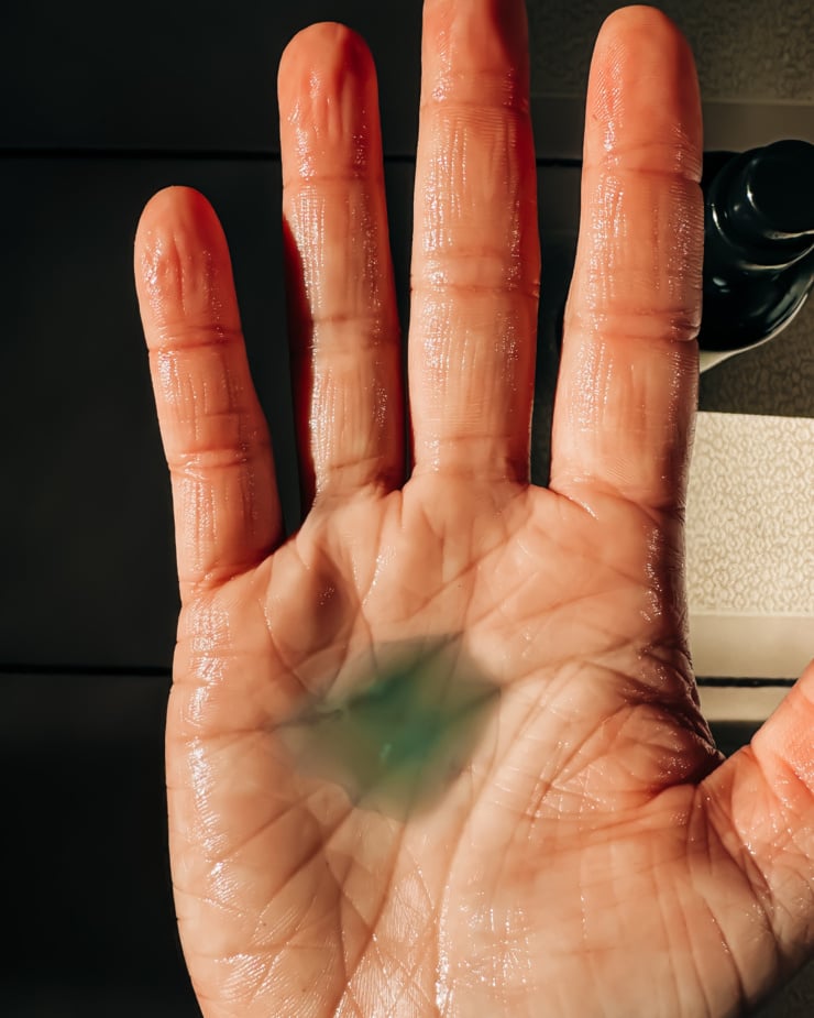 An overhead shot shows a blu-tinged body oil with blue tansy in the palm of a hand.