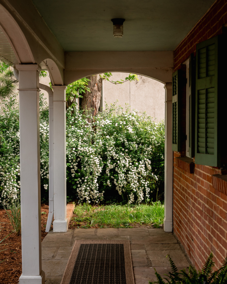 A head-on shot shows a view of blooming bridal veil spirea through the arches of a front porch.