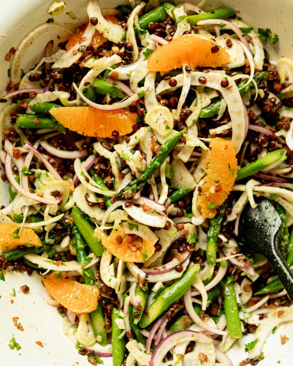 An overhead shot shows a tossed spring french lentil salad with asparagus, fennel, orange, and red onion.