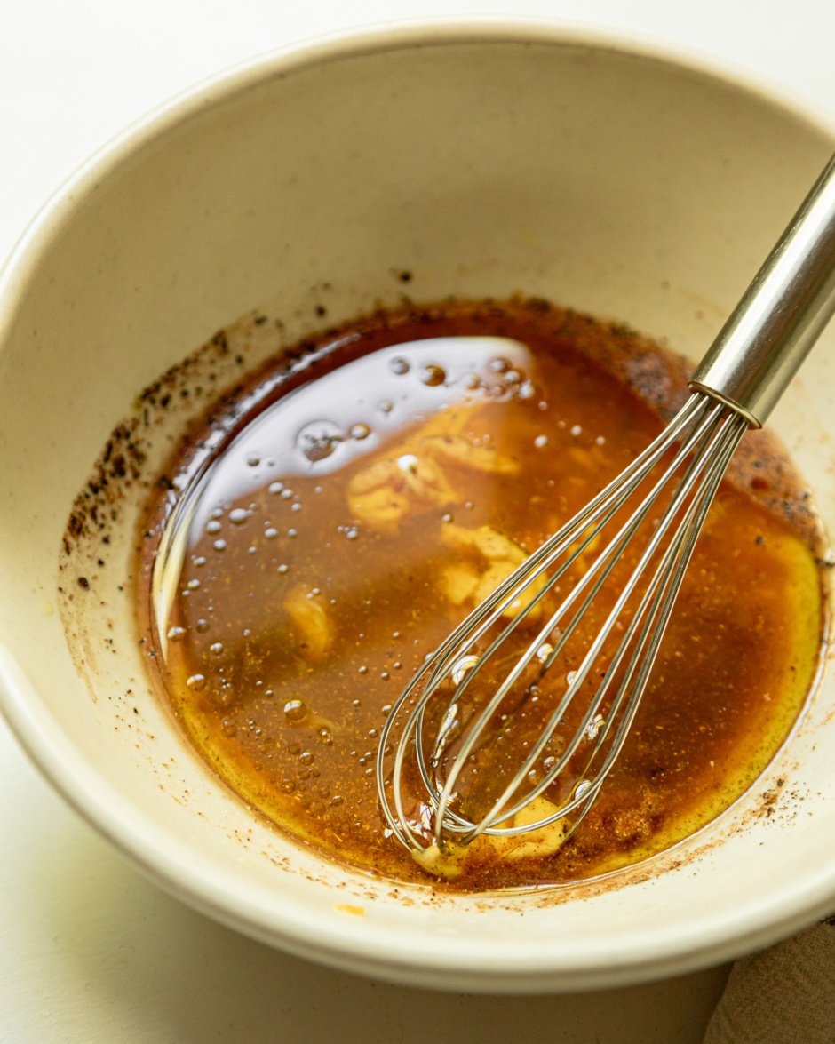 A 3/4 angle shot shows ingredients for a light vinaigrette in a small bowl with a small whisk.