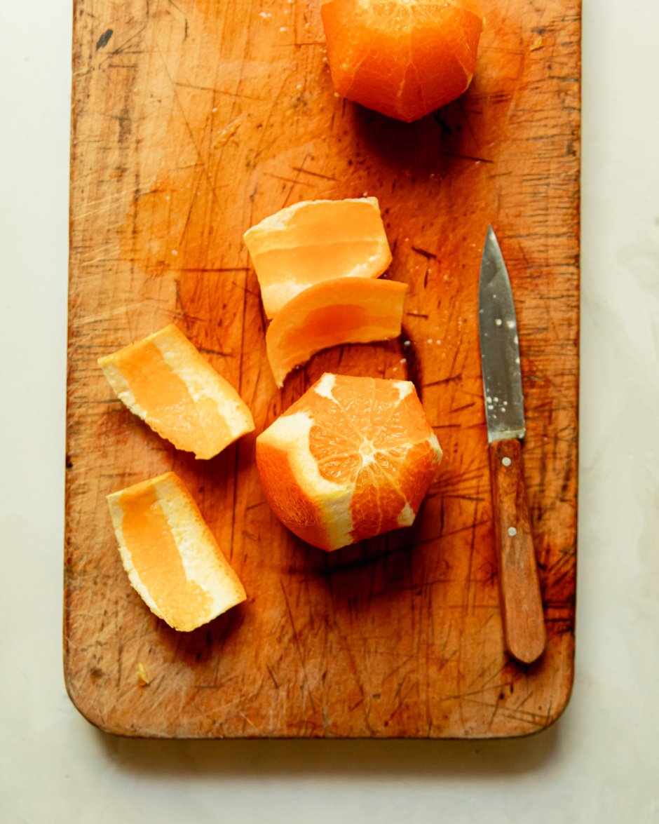 An overhead shot shows an orange in the process of being peeled with a paring knife.
