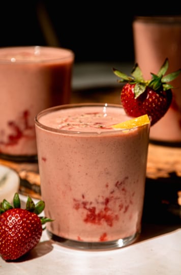 A head-on shot in direct sunlight shows a strawberry lemonade smoothie garnished with a whole strawberry and a little lemon slice.