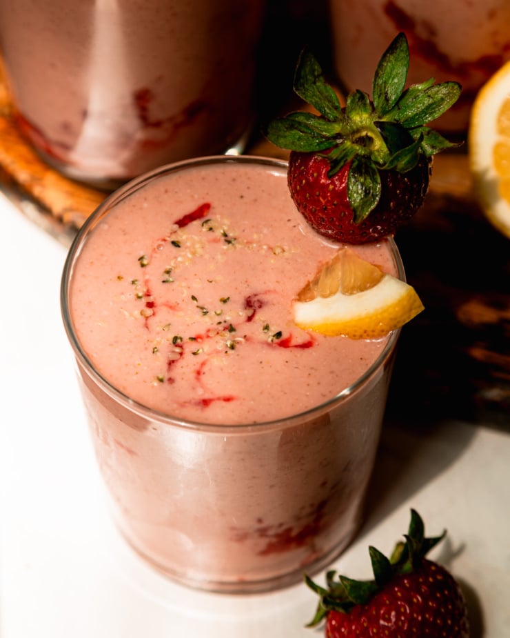 An overhead shot shows a glass of strawberry lemonade smoothie garnished with a little lemon slice and a whole strawberry.