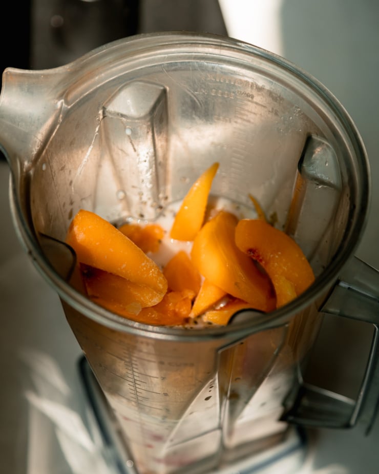An overhead shot shows a blender filled with smoothie ingredients, frozen peaches on top.