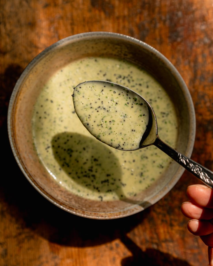 An overhead shot shows a bowl of lemony mint poppy seed dressing. A spoonful is seen up close with little flecks of mint.