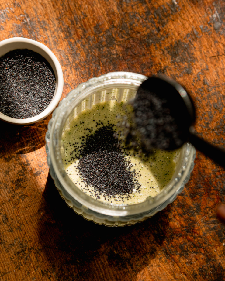 An overhead shot shows poppy seeds being added to a blended up lemony mint dressing.