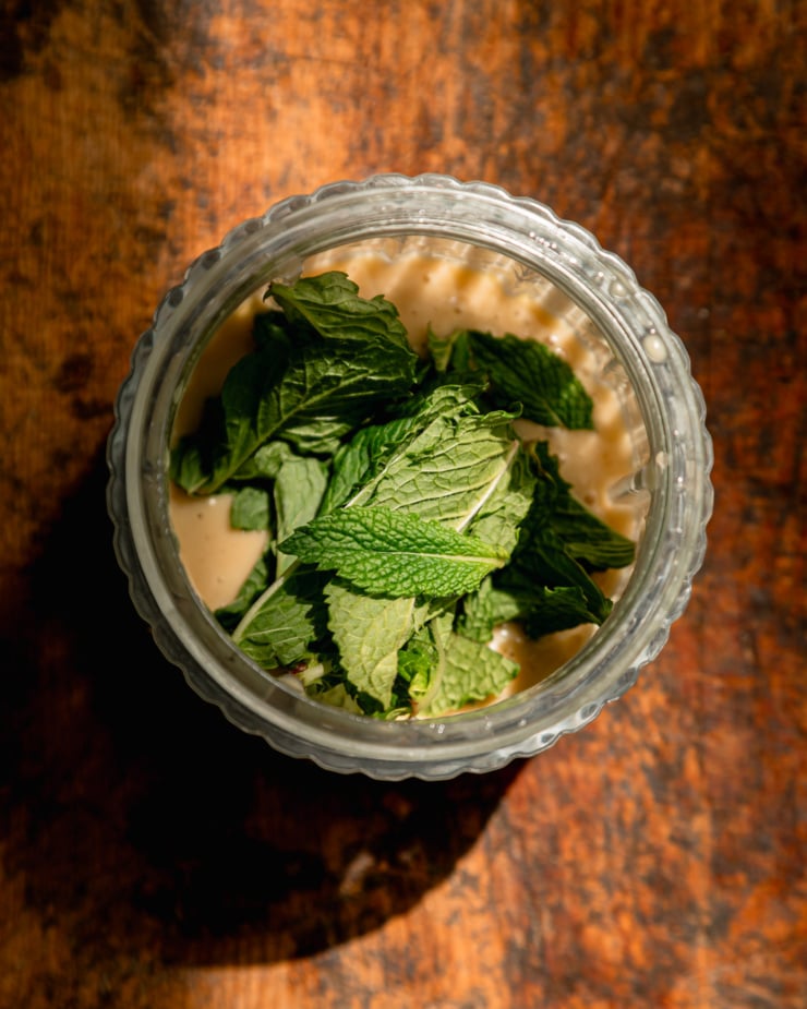An overhead shot shows mint leave son top of a blended up salad dressing in a small blender jar.