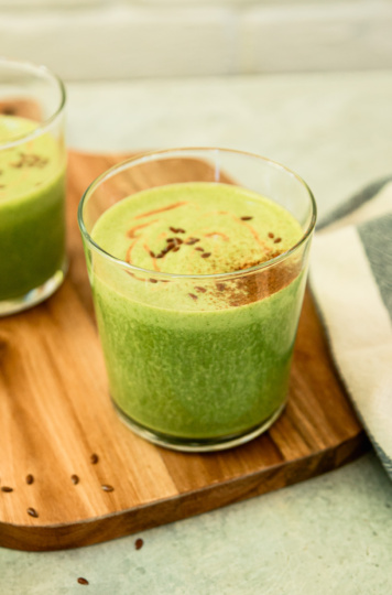 A 3/4 angle shot shows a peanut butter vanilla green smoothie on a wooden board. The top of the smoothie is dusted with cinnamon.