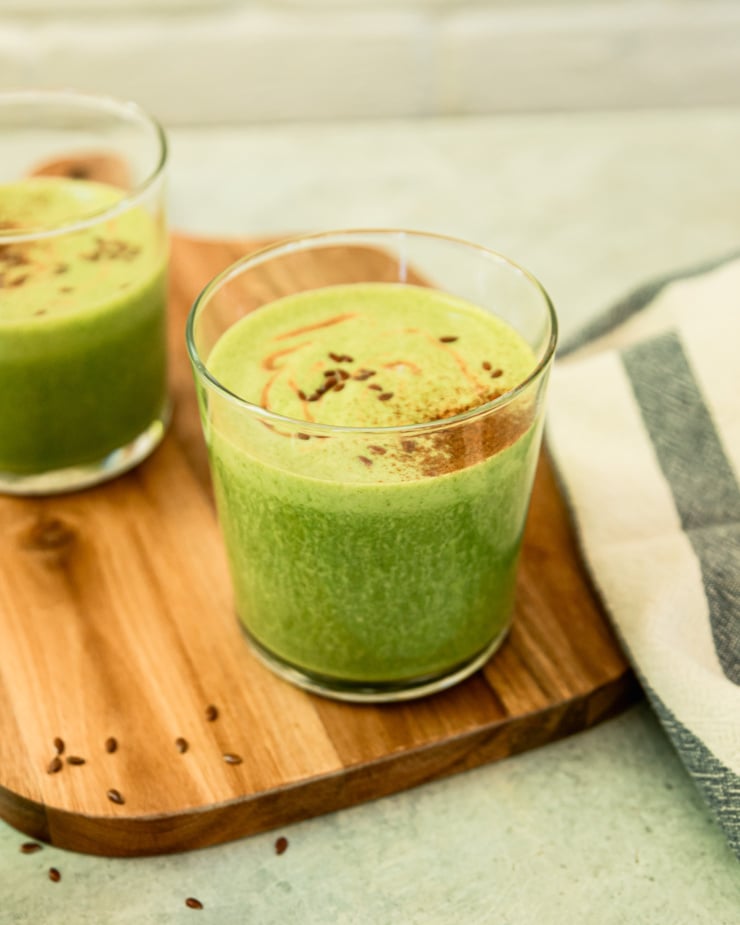 A 3/4 angle shot shows a peanut butter vanilla green smoothie on a wooden board. The top of the smoothie is dusted with cinnamon.