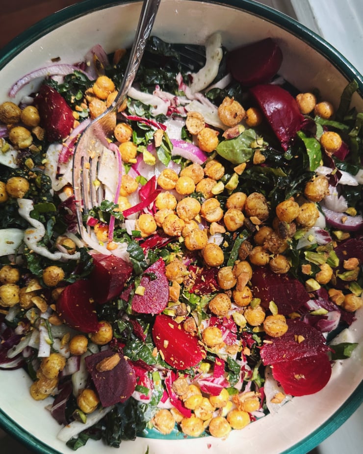 An overhead shot shows a salad in a wide bowl with cooked beets, crispy chickpeas, sliced fennel, sliced kale, red onion, and fresh basil. A fork is sticking out of the bowl.