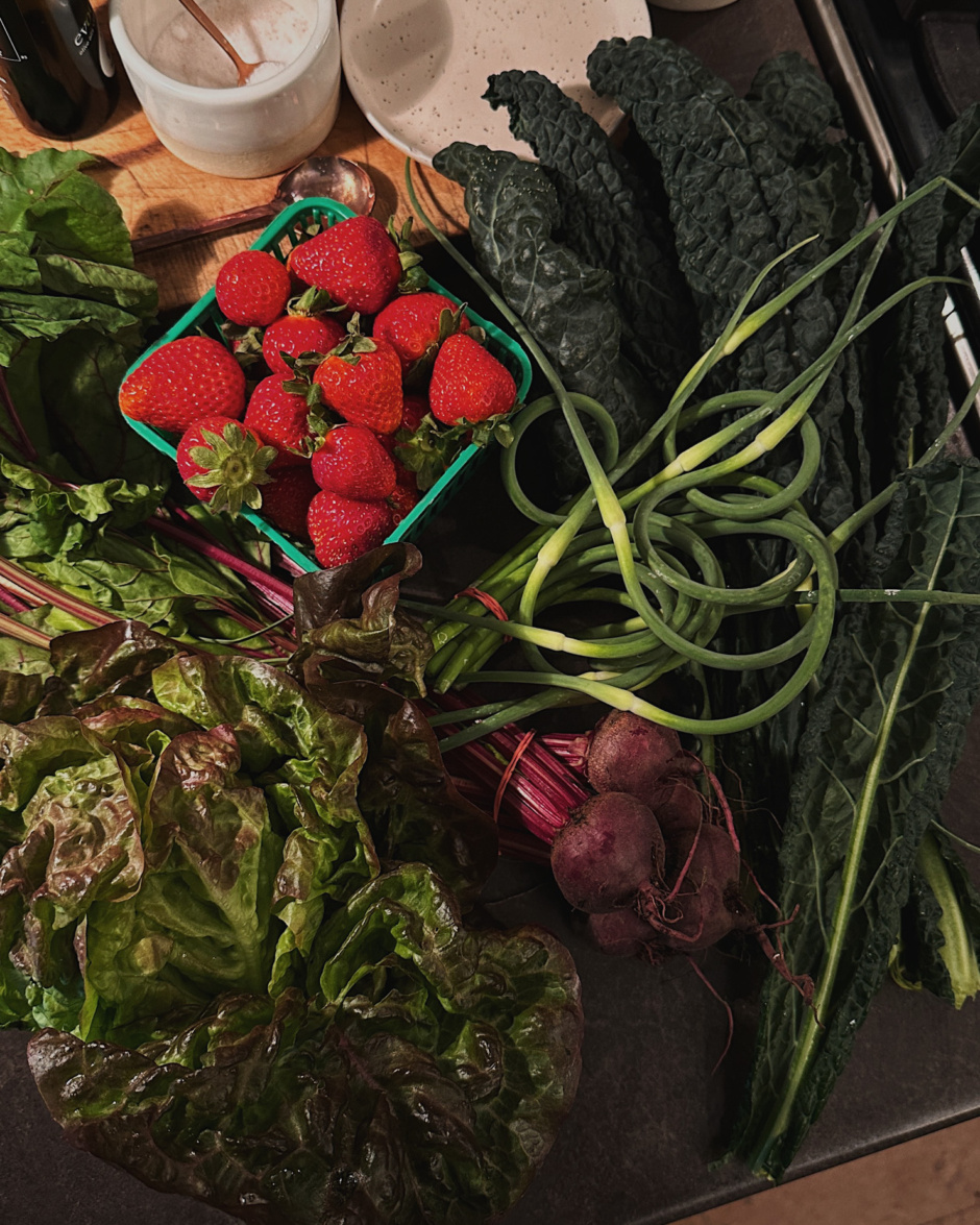 An overhead shot shows a farmer's market haul with strawberries, garlic scapes, lacinato kale, red leaf lettuce, and a bunch of beets.