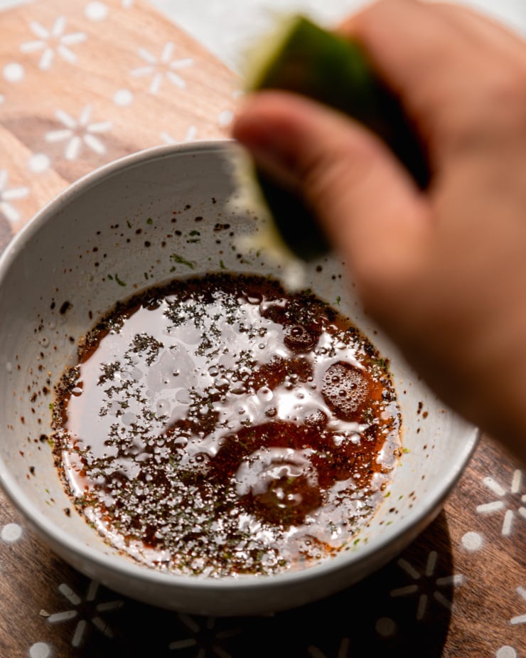 An overhead shot shows a hand squeezing a lime half into a bowl of salad dressing.