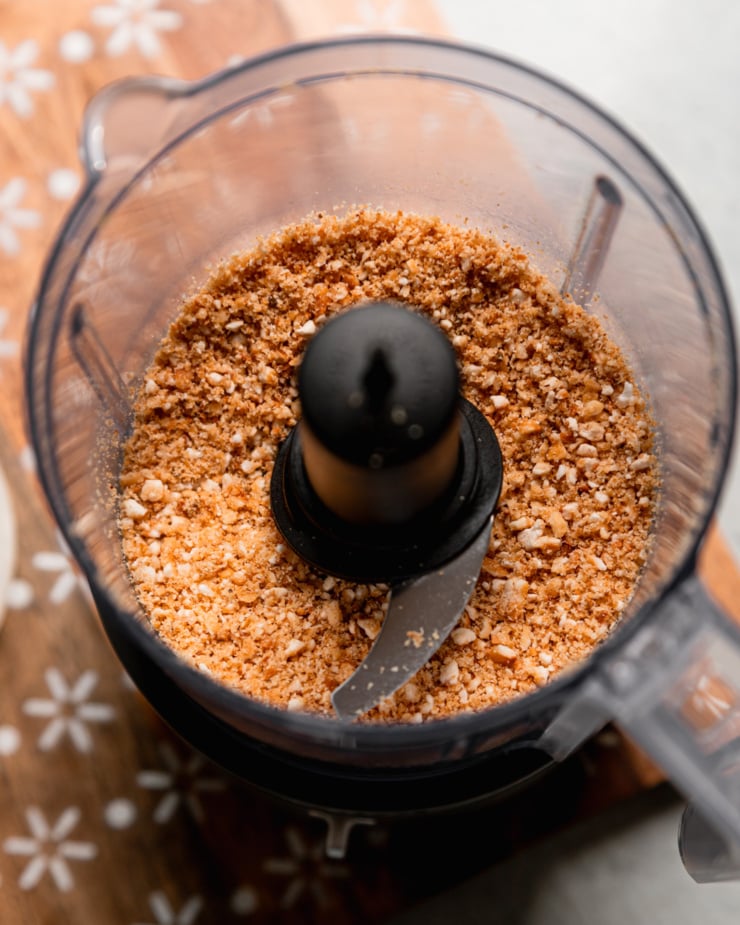 An overhead shot shows finely ground corn nuts in a mini food processor.