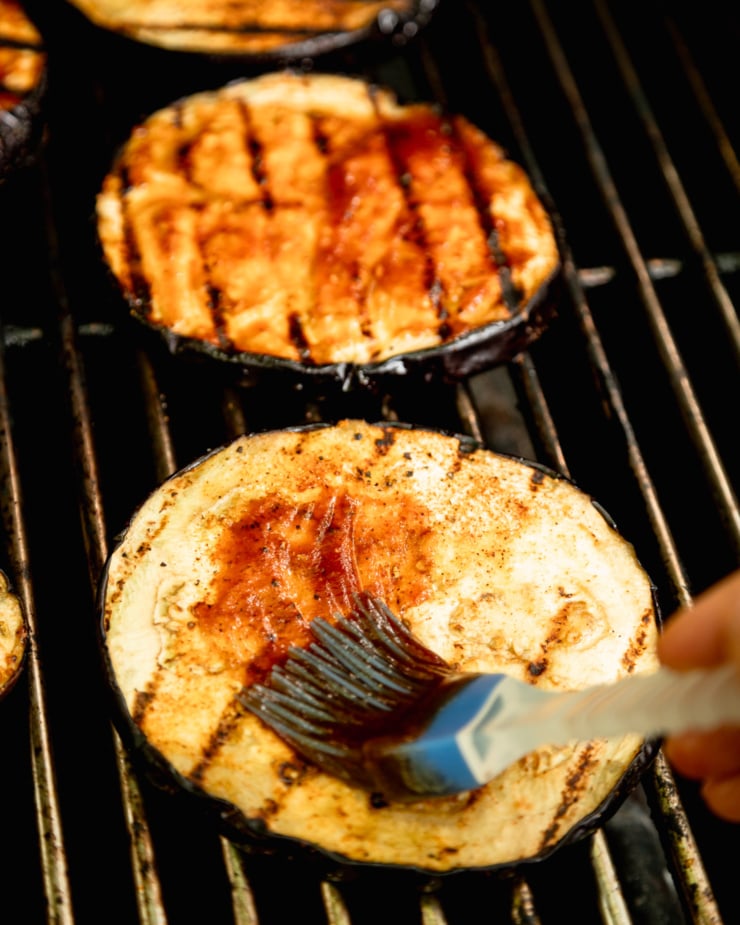 A 3/4 angle image shows eggplant slices on a BBQ being brushed with barbecue sauce.