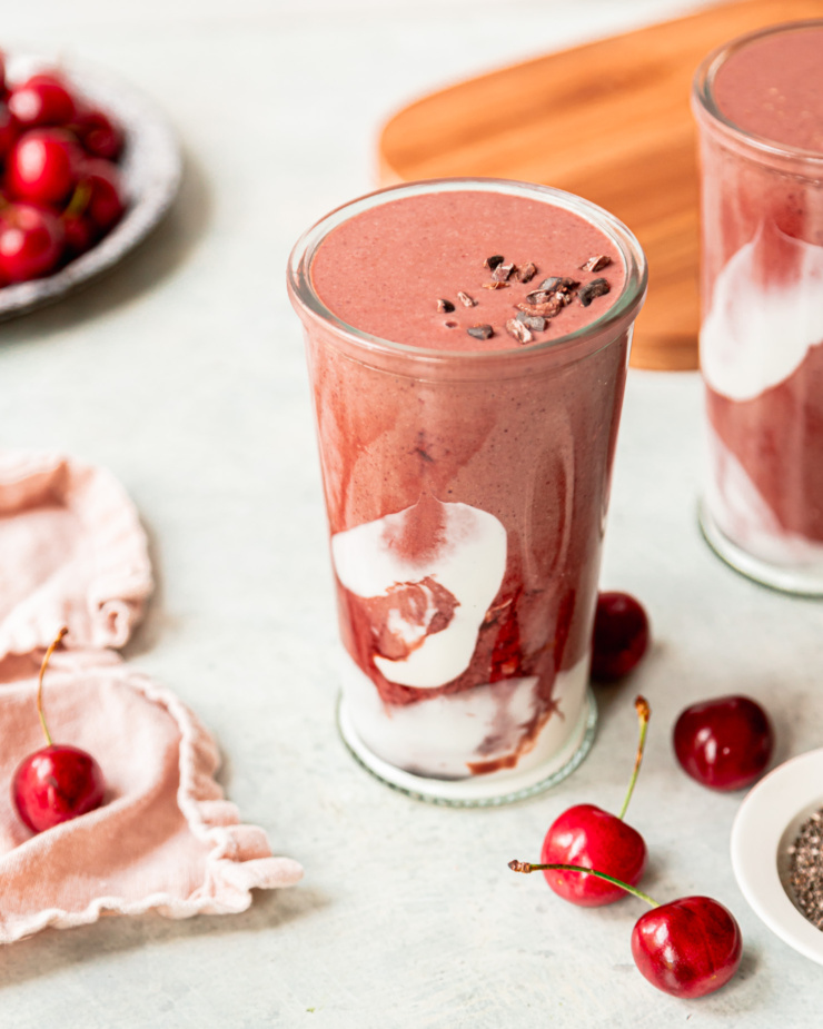 A 3/4 angle shot shows a glass of chocolate cherry smoothie. The glass is swirled with coconut milk yogurt and tart cherry juice concentrate.