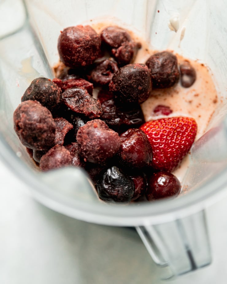 An overhead shot shows fruit and milk in a blender pitcher.