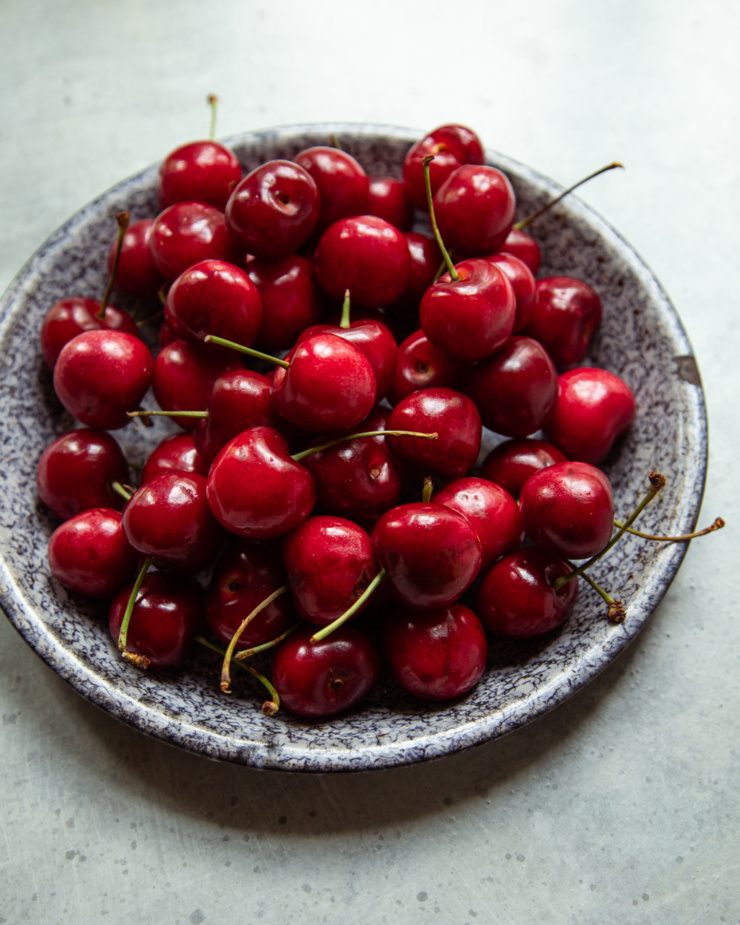 An overhead shot shows fresh cherries in a speckled enamelware plate.