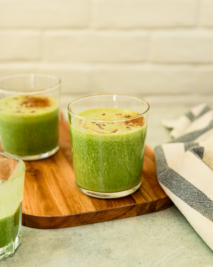 A head-on shot shows a few glasses of peanut butter vanilla green smoothie. Two of the servings are dusted with cinnamon.