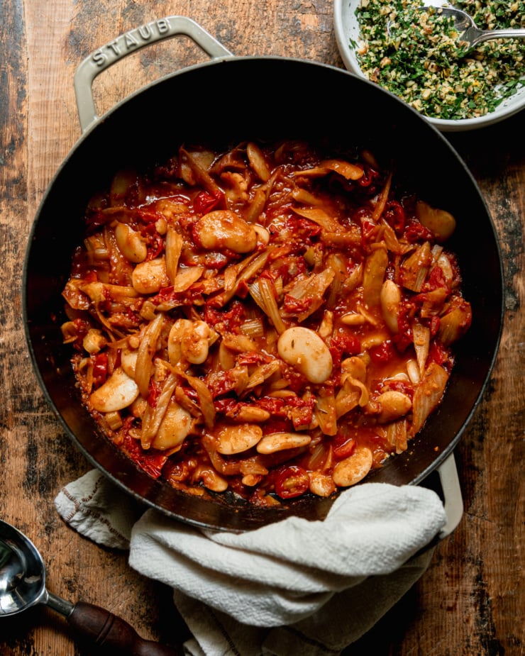 An overhead shot shows a braiser pot filled with a saucy mixture of fennel, tomatoes, and butter beans.