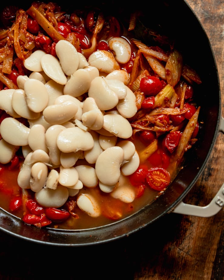 An up close, overhead shot shows a braiser filled with tomato-y fennel, vegetable stock, and butter beans.