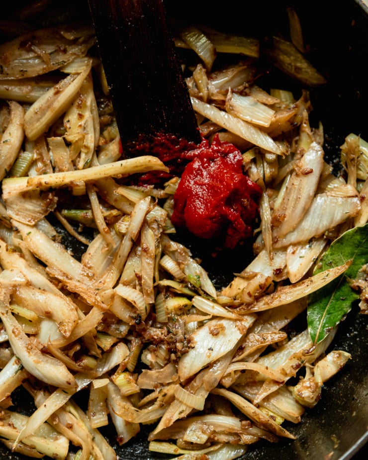 An overhead, up close shot shows caramelized fennel in a pot with a big dollop of tomato paste.