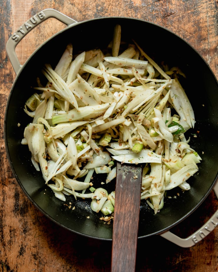 An overhead shot shows a braiser pot filled with sliced fennel and a wooden spatula.