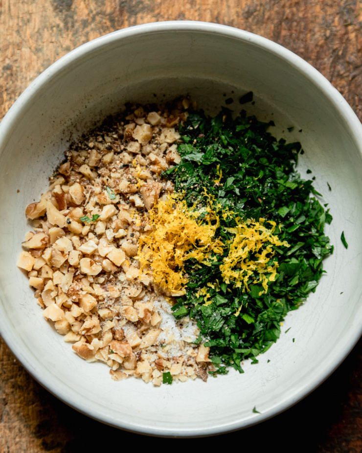 An overhead shot shows a bowl filled with finely chopped walnuts, parsley, and lemon zest.