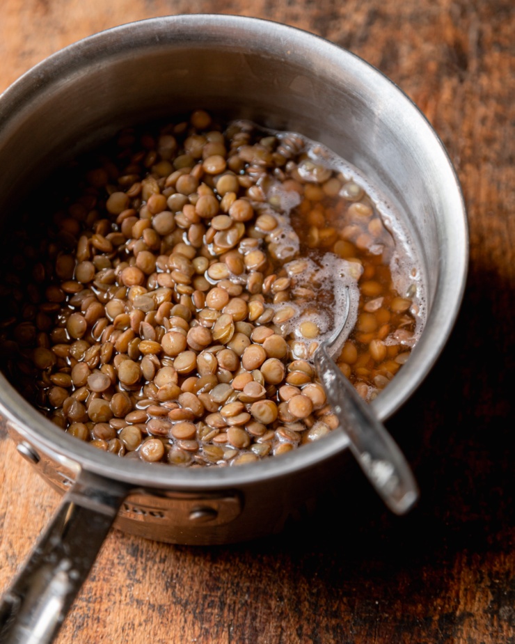 A 3/4 angle shot shows a saucepan filled with cooked lentils with a bit of water and a spoon sticking out.