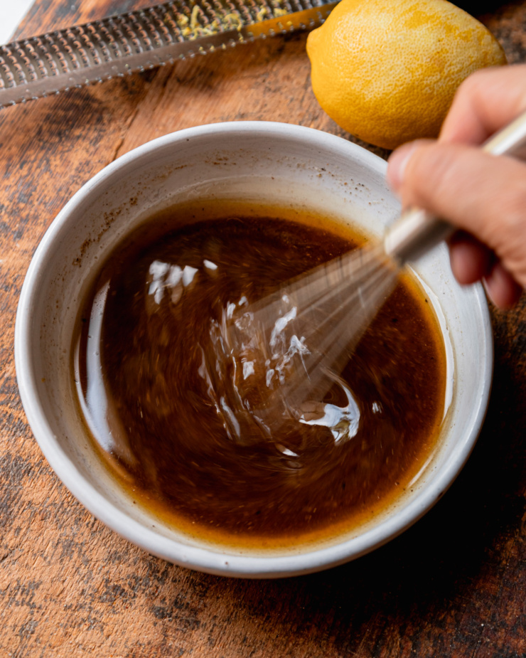 An overhead shot shows a hand using a whisk to bring a spiced lemon dressing together.