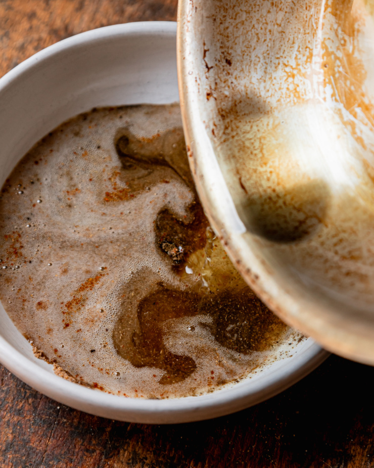 An overhead shot shows hot oil being poured into a bowl with spices.