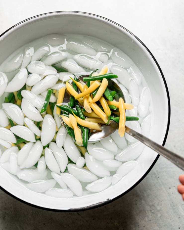 An overhead shot shows boiled string beans being added to an ice water bath to stop the cooking process.